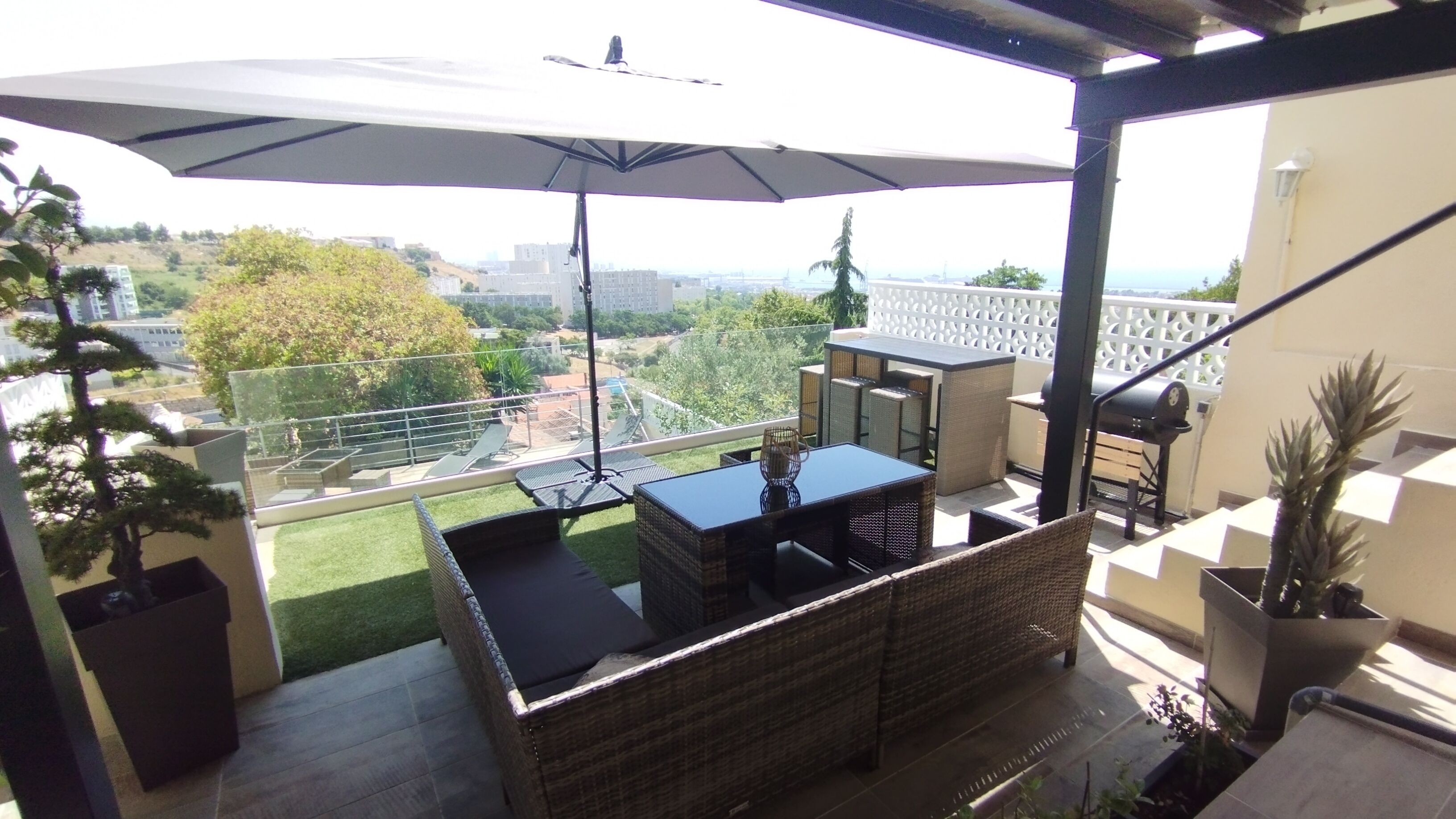 A balcony with outdoor furniture, a large umbrella, and a view of the cityscape.