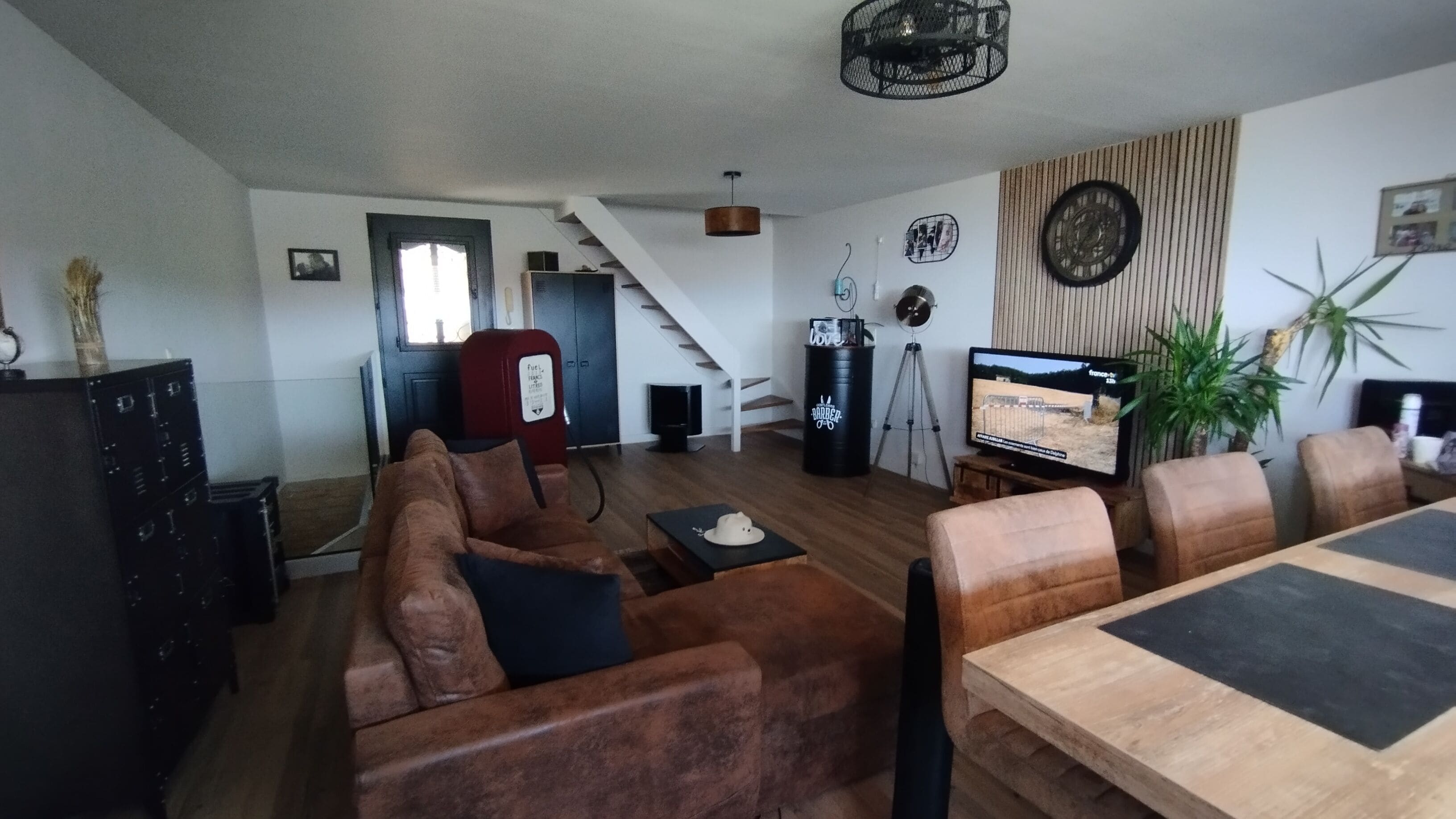A living room with a sofa, a dining table, a television, and a staircase leading to another room.