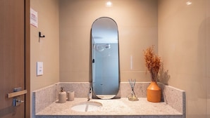 Un bany amb un mirall gran, un lavabo, una tassa i una dutxa.