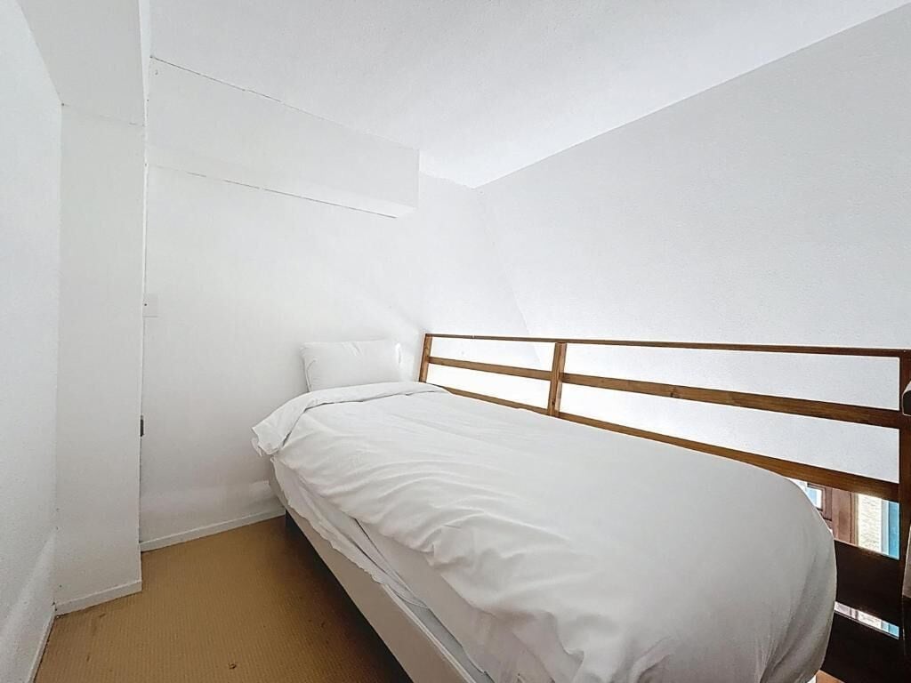 A single bed with a wooden headboard in a room with white walls and a sloped ceiling.
