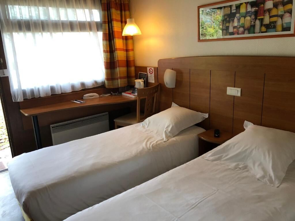 Une chambre d’hôtel avec deux lits, un bureau, une chaise, une lampe et un tableau au mur.