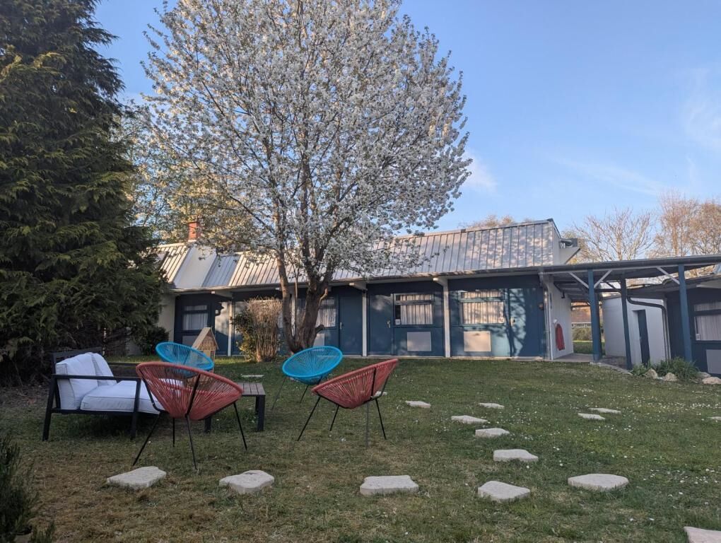 A residential property with a covered outdoor seating area, a tree, and a building with a sloped roof.