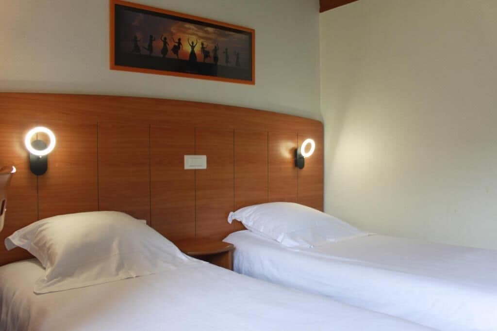 Une chambre d’hôtel avec deux lits, une tête de lit en bois et des lampes de lecture fixées au mur.