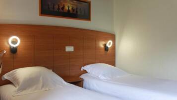 Une chambre d’hôtel avec deux lits, une tête de lit en bois et des lampes de lecture fixées au mur.