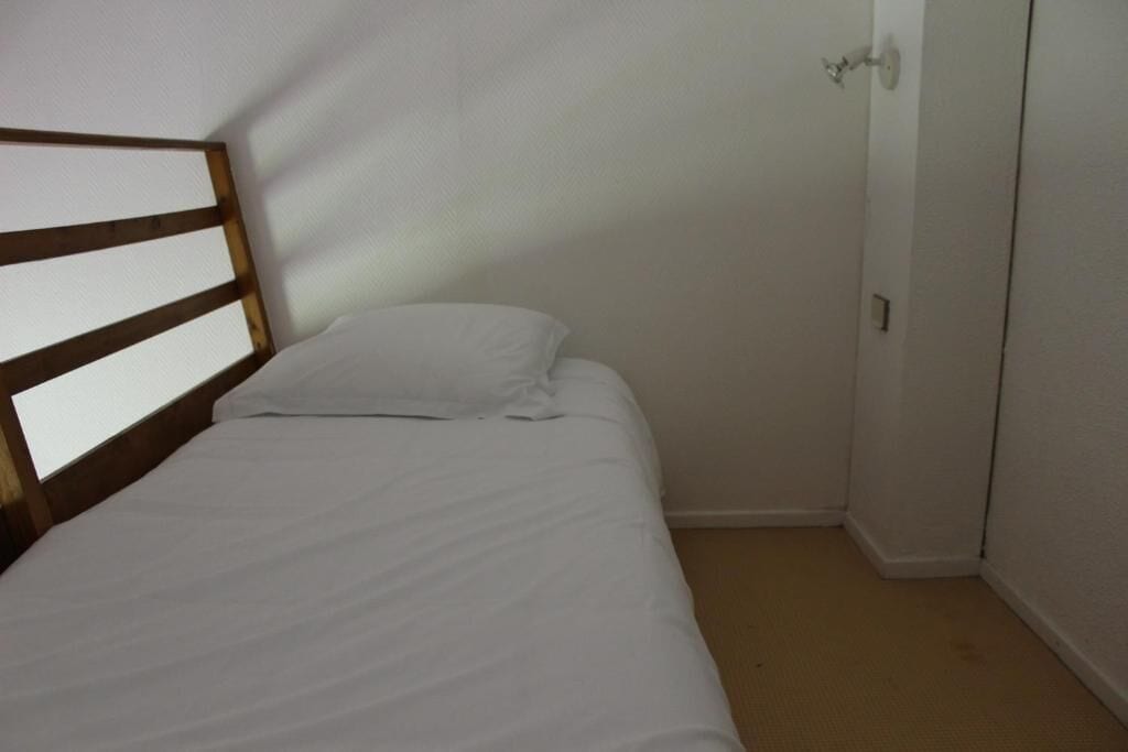 A single bed with a wooden headboard in a small room with a door and a light switch on the wall.
