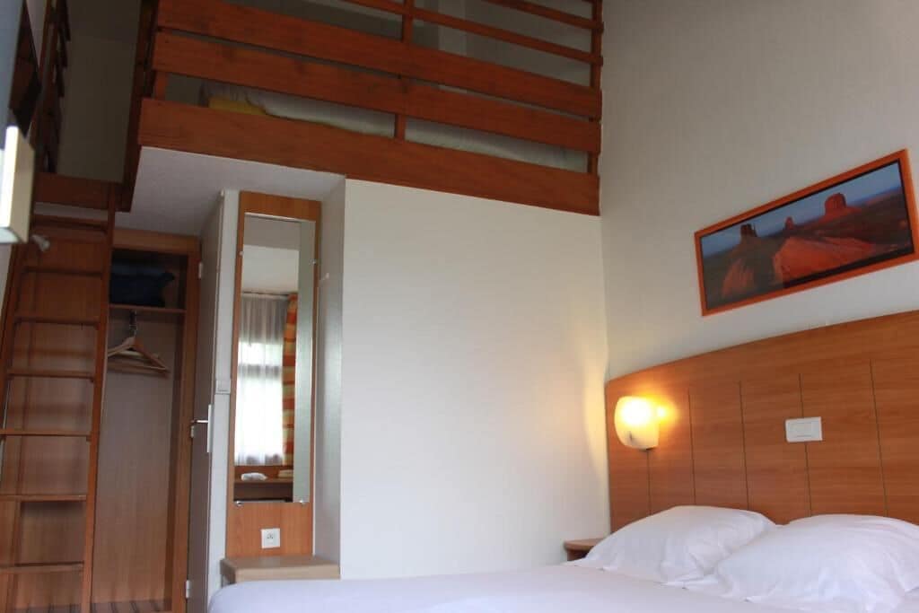 A bedroom with a bunk bed, a wooden headboard, a bedside lamp, and a framed picture on the wall.