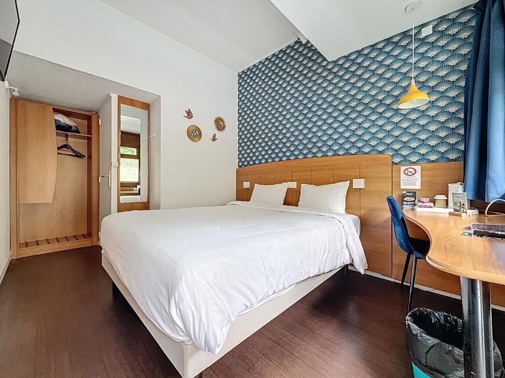 Una habitación de hotel con una cama, un armario de madera, un escritorio con una silla y un papel tapiz estampado.