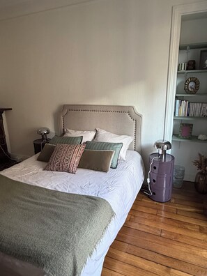 Ein ordentlich bezogenes Bett mit Kissen, einer Nachttischlampe und einem kleinen violetten Gegenstand auf dem Boden.