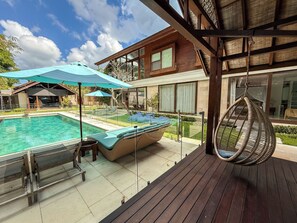 A pool area with a lounge chair and umbrella, a hanging chair, and a wooden deck. - Villa Batu Sari - A Serene Luxury Retreat in the Heart of Canggu (Badung)