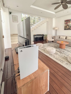Ein Wohnzimmer mit Flachbildfernseher, Holzboden, einer Couch, einem Couchtisch und einer Treppe im Hintergrund.