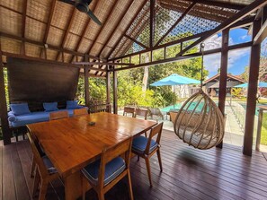 An outdoor wooden deck with a dining table, chairs, and a blue sofa. - Villa Batu Sari - A Serene Luxury Retreat in the Heart of Canggu (Badung)