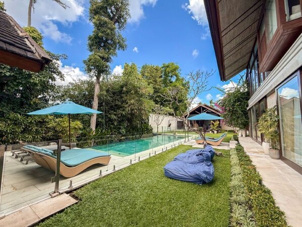 A backyard with a swimming pool, lounge chairs, and a covered seating area. - Villa Batu Sari - A Serene Luxury Retreat in the Heart of Canggu (Badung)