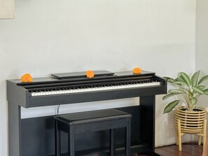 A piano with three orange flowers on top, a black piano stand, and a potted plant beside it. - Villa Batu Sari - A Serene Luxury Retreat in the Heart of Canggu (Badung)