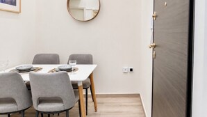 Un coin repas avec une table dressée pour quatre personnes, des chaises grises, un miroir rond accroché au mur et une porte en bois foncé.