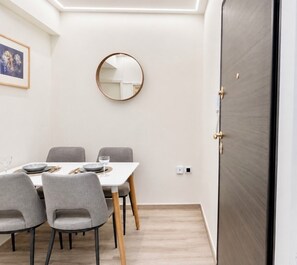 A dining area with a table set for four, grey chairs, a round mirror on the wall, and a dark wooden door.