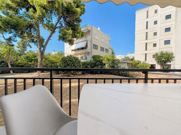 A balcony with a view of a building, trees, and a clear sky.