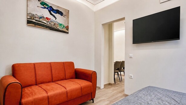 Une pièce comprenant un canapé, un tableau, un téléviseur et une porte donnant sur une autre pièce.