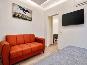 A room with a sofa, a painting, a TV, and a door leading to another room.