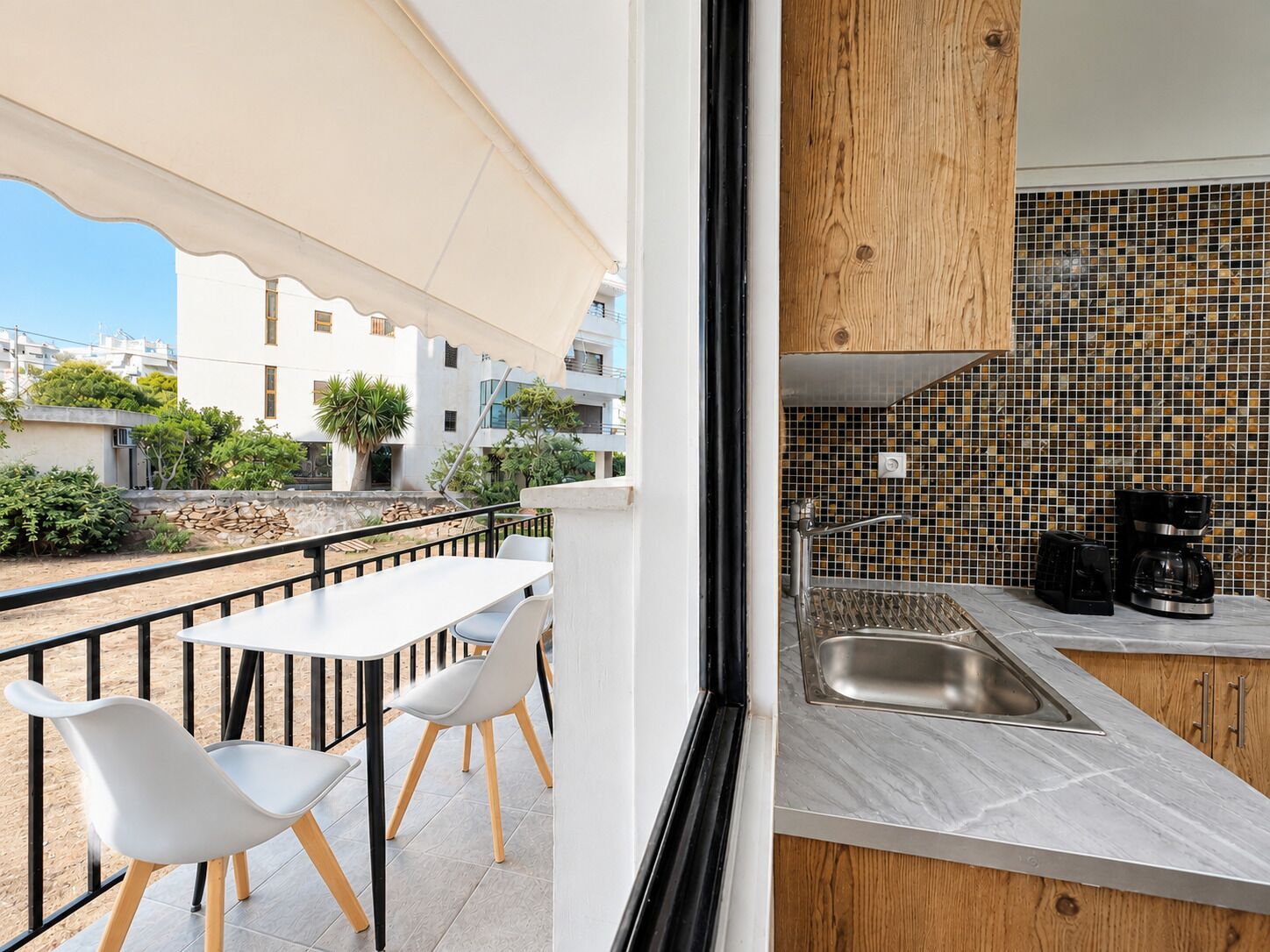 A balcony with a table and chairs, a view of buildings, and a kitchen with a tiled backsplash and modern appliances.