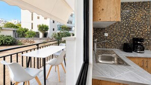 Un balcon avec une table et des chaises, une vue sur les immeubles, et une cuisine dotée d’un plan de travail carrelé et d’appareils électroménagers modernes.