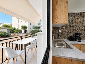 A balcony with a table and chairs, a view of buildings, and a kitchen with a tiled backsplash and modern appliances.