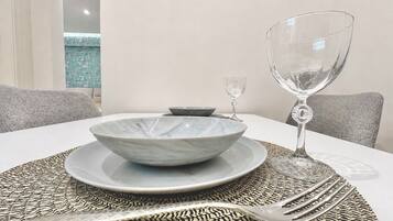 Una mesa para comer con un bol, plato, copa de vino y cubiertos sobre un posavasos tejido.
