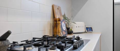 A kitchen with a gas stove, a cutting board, a salt and pepper set, a small potted plant, and a toaster.