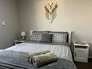 Un dormitorio con cama, dos mesitas de noche, un adorno en la pared y una mesita de noche con lámpara.