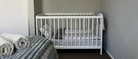 A room with a crib, a bed with rolled towels, a round mirror, and a view through a window.