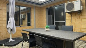 An outdoor patio with a table and chairs, a covered umbrella, and an air conditioning unit on the wall.