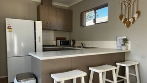 A kitchen with a refrigerator, microwave, stove, and bar stools.