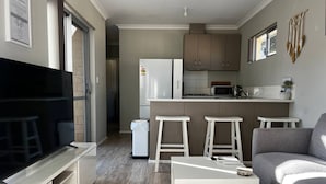 A compact living space with a kitchenette, a seating area with a sofa and bar stools, and a television.