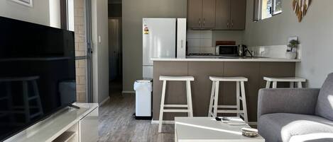 A compact living space with a kitchenette, a seating area with a sofa and bar stools, and a television.