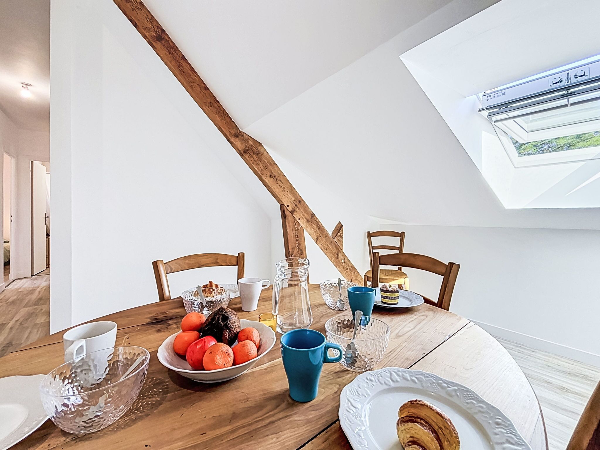 Un espace repas comprenant une table en bois, des chaises et une vue sur l’extérieur grâce à une lucarne.