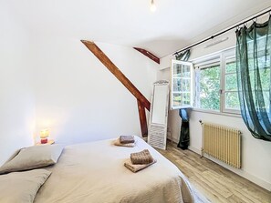 Ein Schlafzimmer mit einem Bett, einem Nachttisch, einem Fenster mit Vorhängen, einer Heizung und einer Holztreppe.