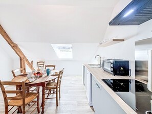A modern kitchen with a dining area, featuring a wooden table, chairs, and a built-in oven. - Gîte de la Grée by Interhome (Saint-Nolff)