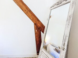 Ein Zimmer mit Holzbalken, einer weißen Wand und einem großen Spiegel mit dekorativem Rahmen.
