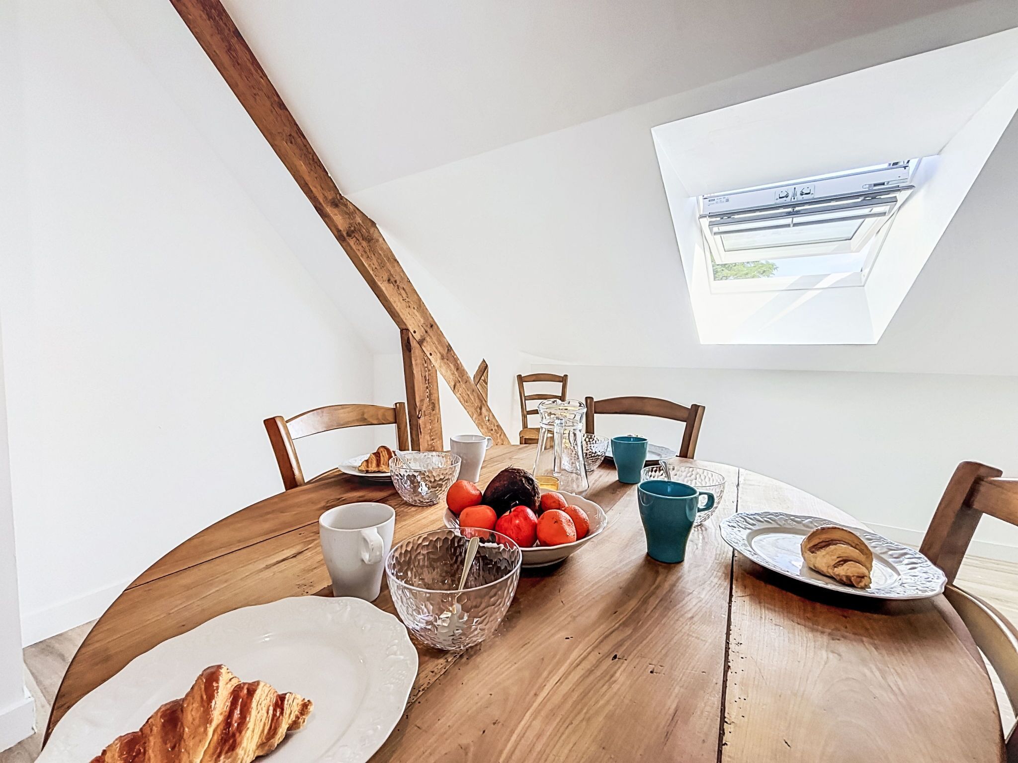 A dining table with breakfast items, a skylight, and wooden beams.
