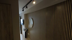 A hallway with wooden flooring, a wall-mounted mirror, and a ceiling light fixture. - Antonio Airport Loft-FREE AIRPORT SHUTLE (Markopoulo Mesogeas)