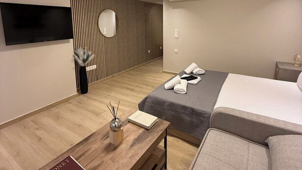A modern hotel room with a bed, bedside table, a mirror, a flat-screen TV, and an air conditioning unit. - Antonio Airport Loft-FREE AIRPORT SHUTLE (Markopoulo Mesogeas)