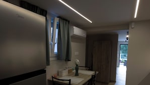 A modern kitchen with a built-in refrigerator, a dining table with chairs, and a window with curtains. - Antonio Airport Loft-FREE AIRPORT SHUTLE (Markopoulo Mesogeas)
