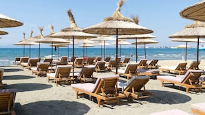A beach with rows of wooden lounge chairs and thatched umbrellas. - Golden Suite Palm Radhime (Orikum)
