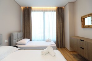 Ein Hotelzimmer mit zwei Betten, einem Holzschrank und einem großen Fenster mit Vorhängen.