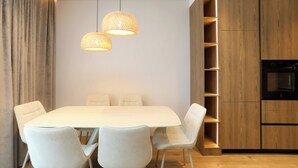 A modern dining area with a white table, four chairs, and two hanging pendant lights. - Golden Suite Palm Radhime (Orikum)