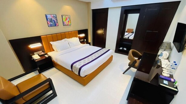 A modern hotel room with a bed, a desk, a chair, and artwork on the walls.
