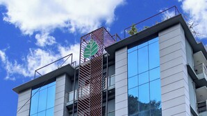 A modern hotel building with a prominent green leaf logo, large reflective windows, and a sign indicating a hotel and resort.