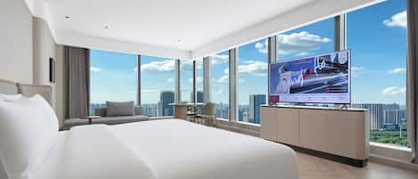 A modern hotel room with a large bed, a TV mounted on the wall, and a city view through large windows.