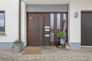 Puerta de madera con un panel de vidrio, felpudo y planta en maceta en los escalones.