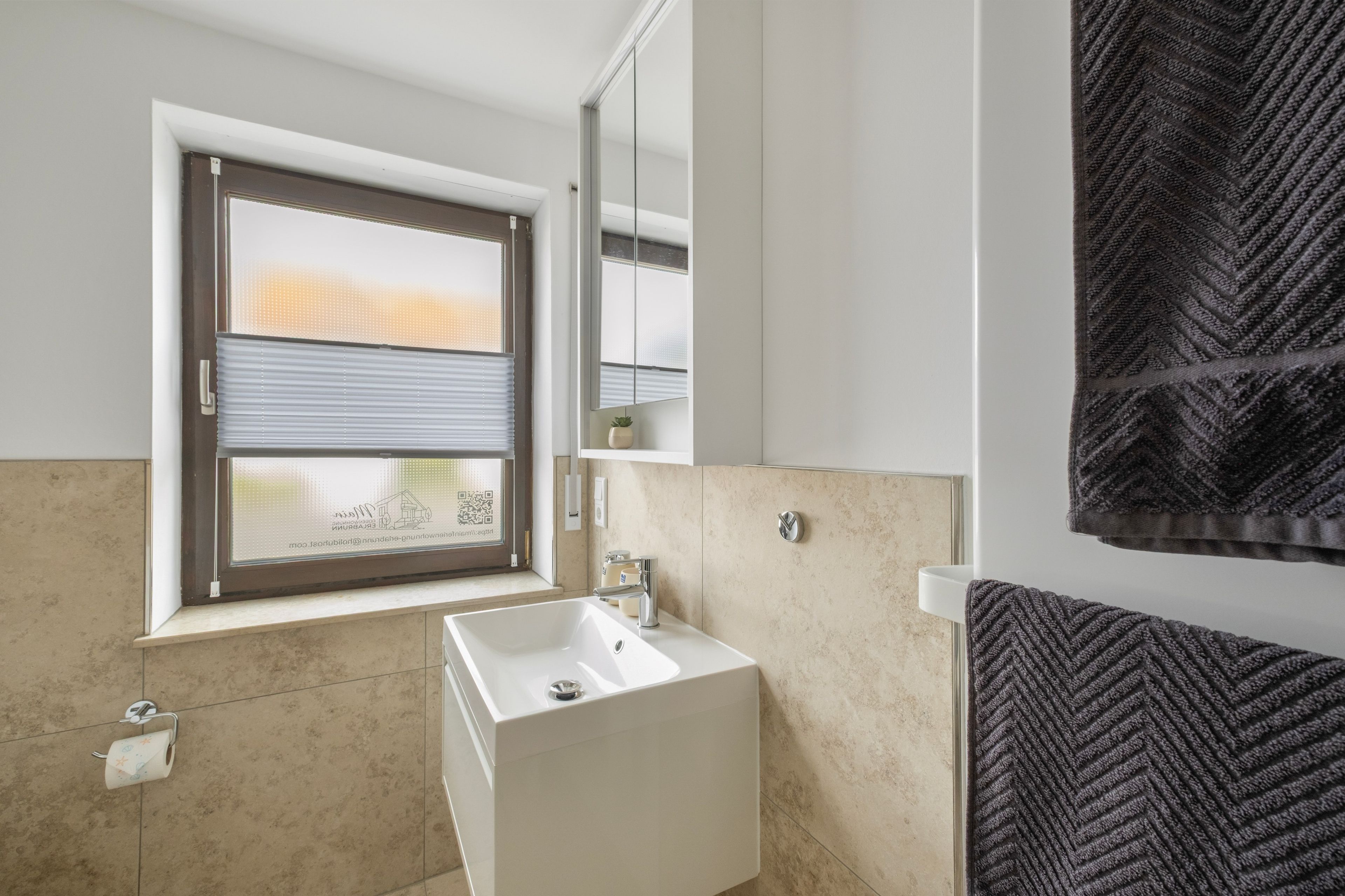 Une salle de bain avec une fenêtre, un lavabo, une serviette et un miroir.