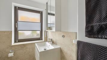 Une salle de bain avec une fenêtre, un lavabo, une serviette et un miroir.